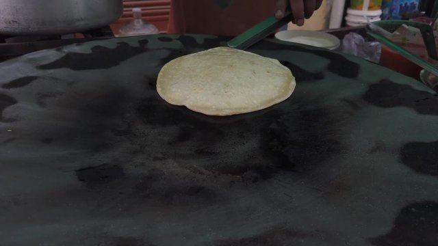 Slow-motion of hands cooking making flipping traditional Indian flat bread, Parotta or Chapatti, with stuffed eggs on large open heated metal pan on the street side in Delhi, handheld stabilized 4k 