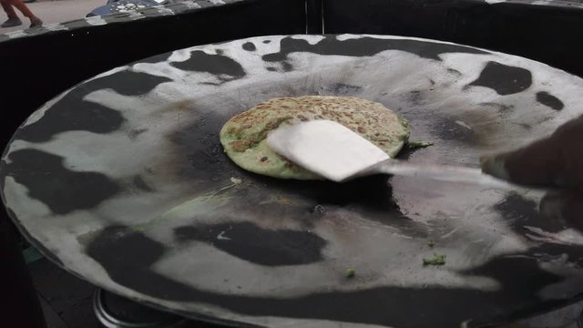 Slow-motion of hands cooking making flipping traditional Indian flat bread, Parotta or Chapatti, with stuffed eggs on large open heated metal pan on the street side in Delhi, handheld stabilized 4k 