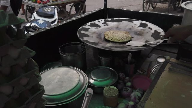 Slow-motion of hands cooking making flipping traditional Indian flat bread, Parotta or Chapatti, with stuffed eggs on large open heated metal pan on the street side in Delhi, handheld stabilized 4k 