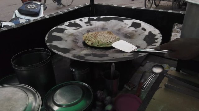 Slow-motion of hands cooking making flipping traditional Indian flat bread, Parotta or Chapatti, with stuffed eggs on large open heated metal pan on the street side in Delhi, handheld stabilized 4k 