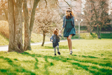 young and stylish mother with long hair and a jeans jacket playing with her little cute daughter in the summer park