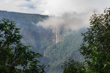 waterfall falling from a great height rocky mountains overgrown jungles and cloud-covered