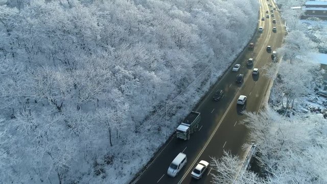 Aerial forward asphalt acive road traffic cars snow white trees frozen forest fabulous cityscape countryside highway serpentine. Sunny day. Russia cold winter season north Siberia Europe