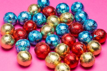 Fototapeta na wymiar Chocolates in a multi-colored foil on a pink background