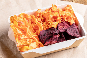 Small paper box with vegetable chips on wrapping paper. 