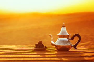 Arabian teapot and dates in the desert at a beautiful sunset symbolizing Ramadan