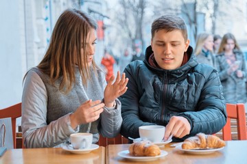 Young friends man and woman talking in outdoor cafe drinking tea coffee with croissants
