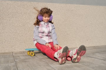 Little girl rides a skateboard, in area near the house, spring season, gray wall background