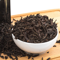Dried tea is poured into a ceramic cup on a wooden board on a white background.