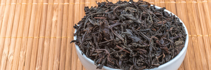 Dried tea is poured into a ceramic cup on a bamboo mat.