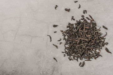 Dried tea is poured scattered on a grey textured background.