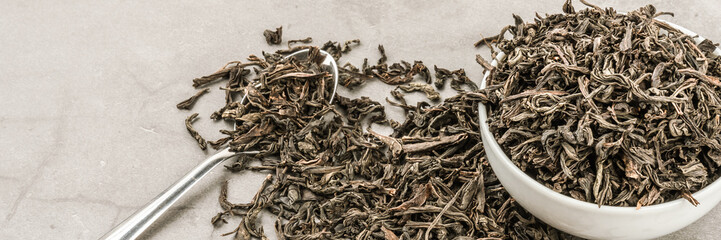 Dried tea in a white ceramic cup with a spoon on a gray textured background.