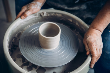 Master on potter wheel makes clay dishes. Workshop place