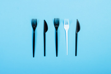 Black plastic forks and knives and one white plastic fork on a blue background. Concept plastic, harmful, environmental pollution, stop plastic. Flat lay, top view.