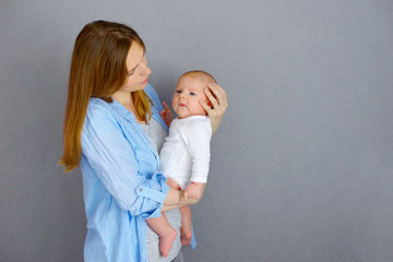 Happy mother's day. Happy mom and baby infant 2 months old boy at grey background. Newborn baby health, breastfeeding, medicine and international holidays concept.