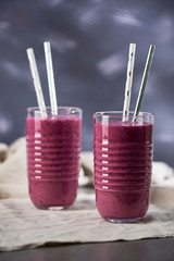 Two glasses with two straws full of violet smoothie on linen canvas