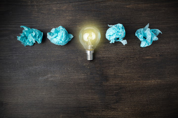 great idea concept with crumpled light blue paper and light bulb on wooden background