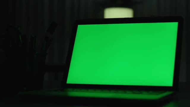 Laptop with green screen. Dark office.  Perfect to put your own image or video.Green screen of technology being used. Chroma Key laptop