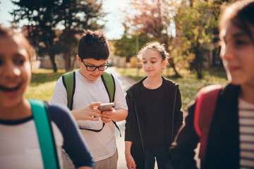 Boy going to school with classmates and using smart phone at schoolyard