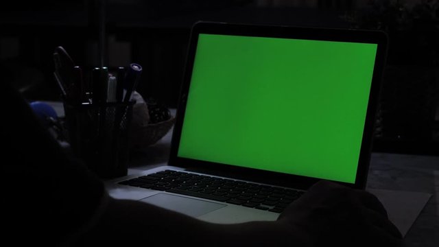 Laptop with green screen. Dark office.  Perfect to put your own image or video.Green screen of technology being used. Chroma Key laptop