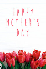 Happy Mother's Day text and beautiful red tulips on white wooden background flat lay. Happy mother day greeting card with spring flowers. Stylish simple holiday card