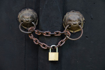 Ancient door with a lion head knocker are locked by an old chain and padlock.