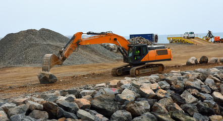 Digger moving large boulders on construction site.
