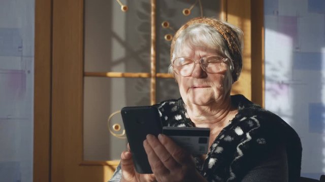 An old woman using a smartphone and a credit card examines payment documents. Social inequality