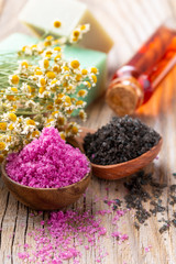 Sea salt in bowl, aroma oil in bottles, Wellness and flowers on grey textured background and flowers on vintage wooden background. Selective focus.