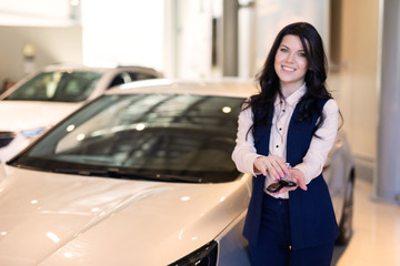 Fototapeta na wymiar Happy woman buyer possing with keys near her new vehicle in car dealership