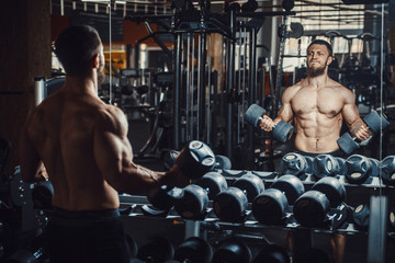 Good looking young man bodybuilder lifting dumbbells and working on his biceps focused in front of...