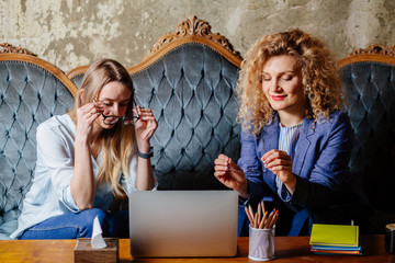 Two female friends working together at cafe, using computer, drinking coffee and sharing Ideas. Smiling women wearing eyeglasses talking about project. business people team work concept.