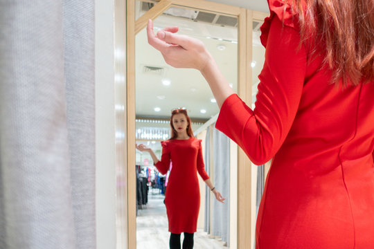 young girl tries on a red dress in a fitting room boutique. woman buys clothes in the store.