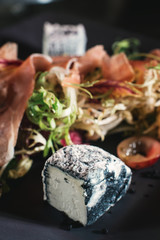 Fototapeta na wymiar Fresh salad with prosciutto, tomato, lettuce and blue cheese on a stone plate