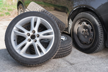 Fototapeta na wymiar Summer wheels lying near car on winter tires. Seasonal tyre change abstract concept.