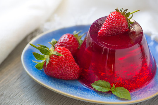 Photo of fruit jelly with fresh strawberry. Healthy food. Strawberry jelly on white plate. Summer dessert with fruit jelly and fresh strawberry.