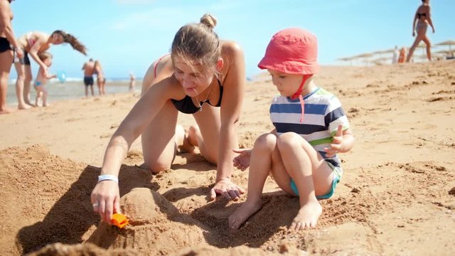 4k video of young mother with her child son playing with toy car on the sea beach. Family relaxing during summer beach vacation