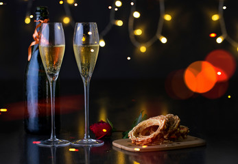 A pair of glasses of champagne with a rose on a table, a sweet cake and a bottle of champagne. festive picture.