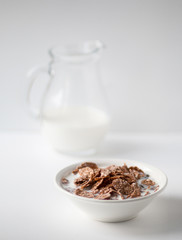 Bowl of multigrain natural flakes and milk jug on a white background. Healthy food. Side view.