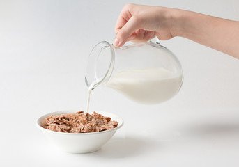 Pouring milk into the bowl with multigrain natural flakes on a white background. Healthy food. 