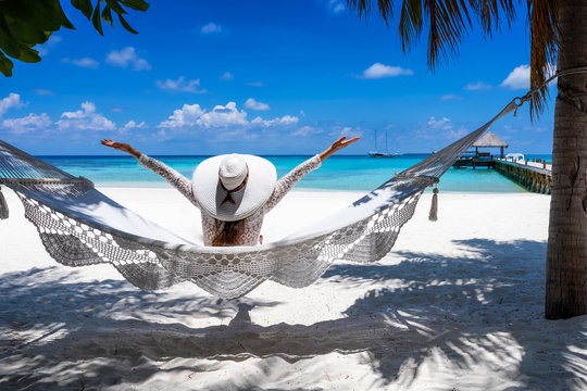 Gl&uuml;ckliche Frau mit Sonnenhut auf einer H&auml;ngematte genie&szlig;t die Aussicht auf einen tropischen Strand auf den Malediven