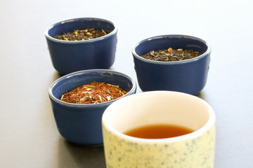 Cup of tea in front of different sorts of tea leaves in bowls on white background. Modern minimalistic image
