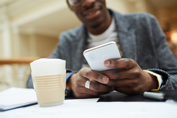 Mid section portrait of contemporary African-American man studying sitting at table in cafe and using smartphone, copy space