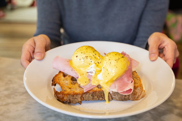 Female hands holding plate with egg Benedict, breakfast meal.