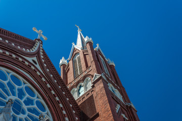 Fototapeta na wymiar Beautiful details of steeples and rose window, Gothic Revival church, red brick white crosses, blue sky, horizontal aspect