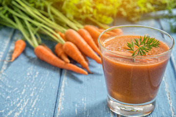 Fresh carrot smoothie in glass on rustic wooden background.