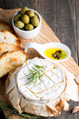 Baked camembert cheese. Fresh Brie cheese and a slice on a wooden board with nuts, honey, rosemary, baguette bread grilled toasts and leaves. Brie type of cheese. Italian, French cheese.