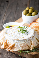 Baked camembert cheese. Fresh Brie cheese and a slice on a wooden board with nuts, honey, rosemary, baguette bread grilled toasts and leaves. Brie type of cheese. Italian, French cheese.