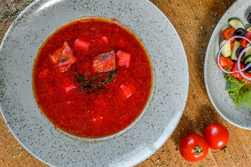 Ukrainian red borsch; red soup in a plate; food photography; home Ukrainian cuisine; for the cafe menu; business lunch; fatty foods; plates of food are on the wooden table;