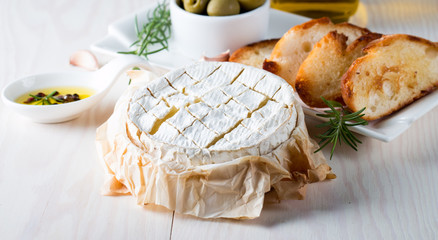 Baked camembert cheese. Fresh Brie cheese and a slice on a wooden board with nuts, honey, rosemary, baguette bread grilled toasts and leaves. Brie type of cheese. Italian, French cheese.